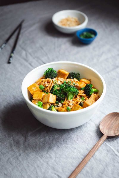 Spicy noodles with tofu and broccoli in a serving bowl next to a wood spoon.