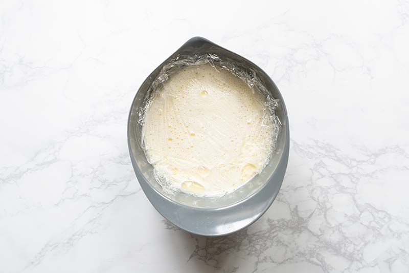 Gelato base in a bowl with plastic wrap pressed directly against the base