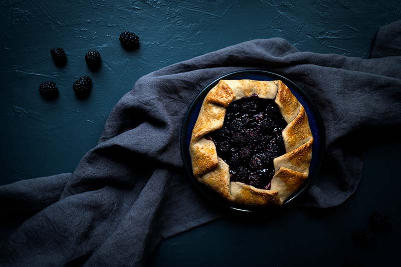 Blackberry galette on a plate surrounded by blackberries