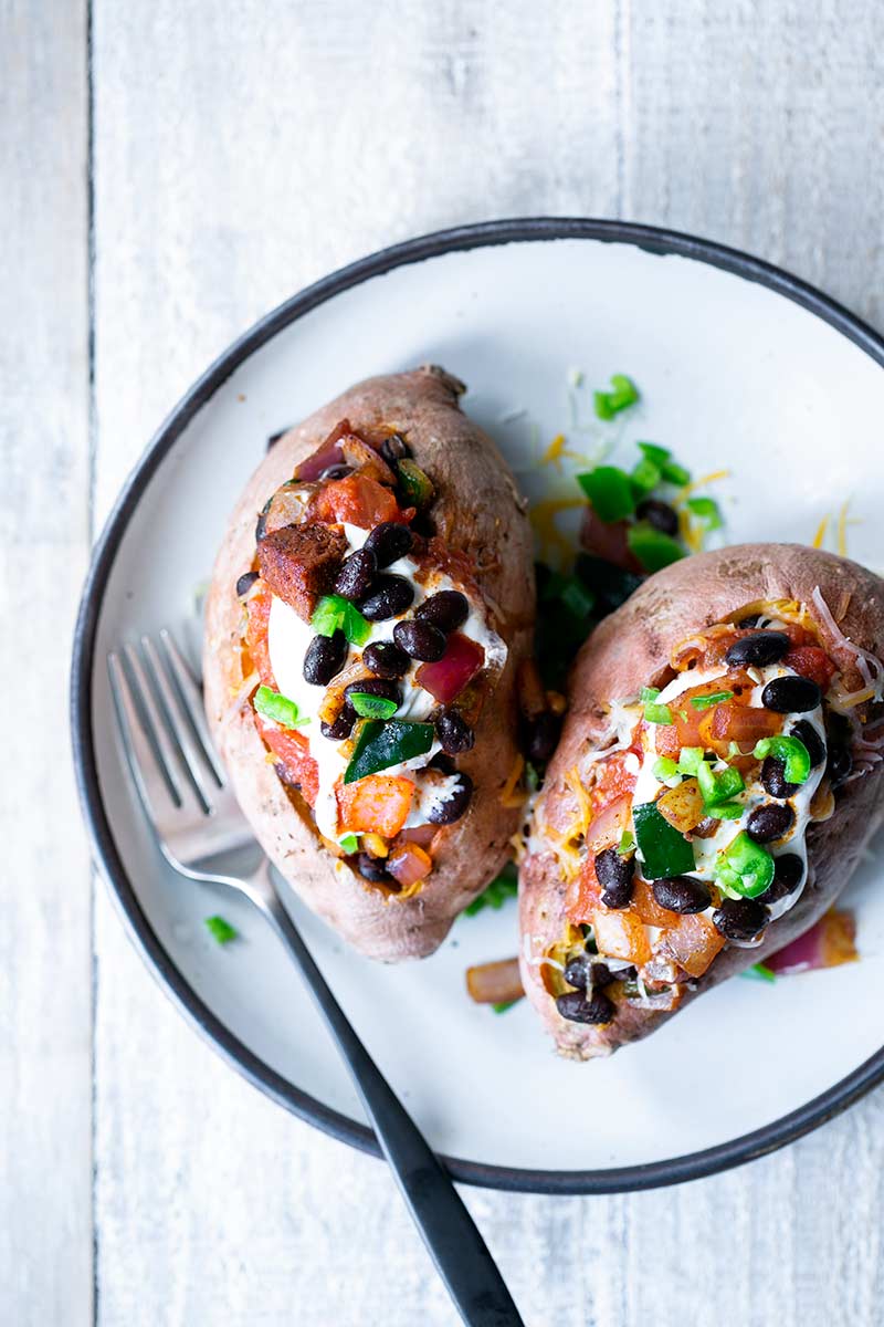 Two loaded sweet potatoes on a plate with a fork