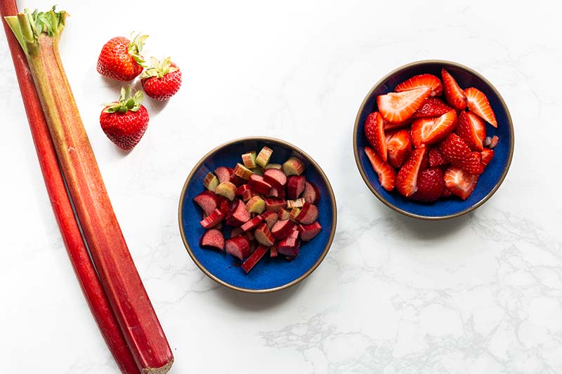 Chopped strawberries and rhubarb in separate blue bowls